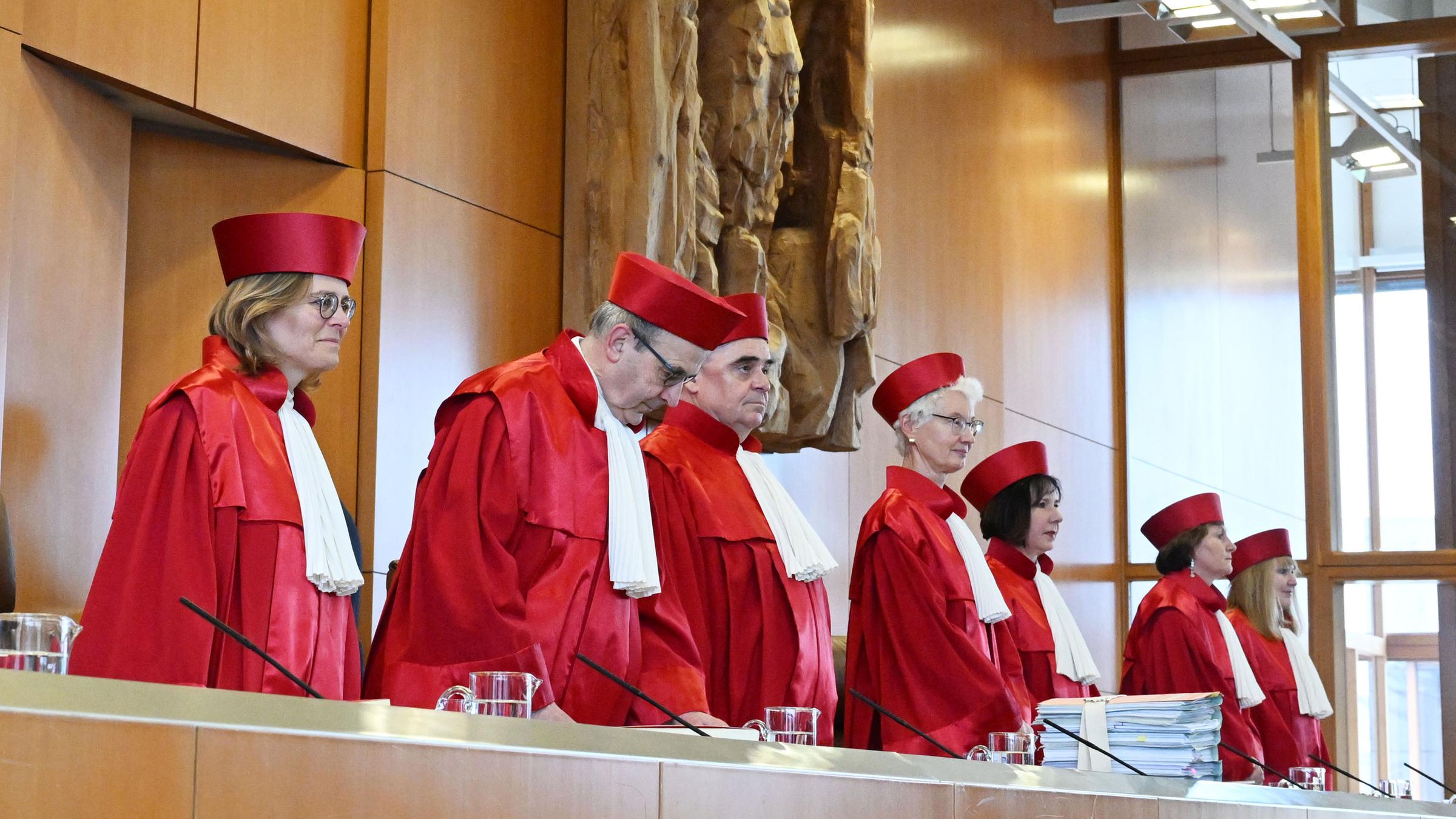 Mehrere Richter stehend in roter Robe. Hinter ihnen eine Wand mit einer steinernen Skulptur.