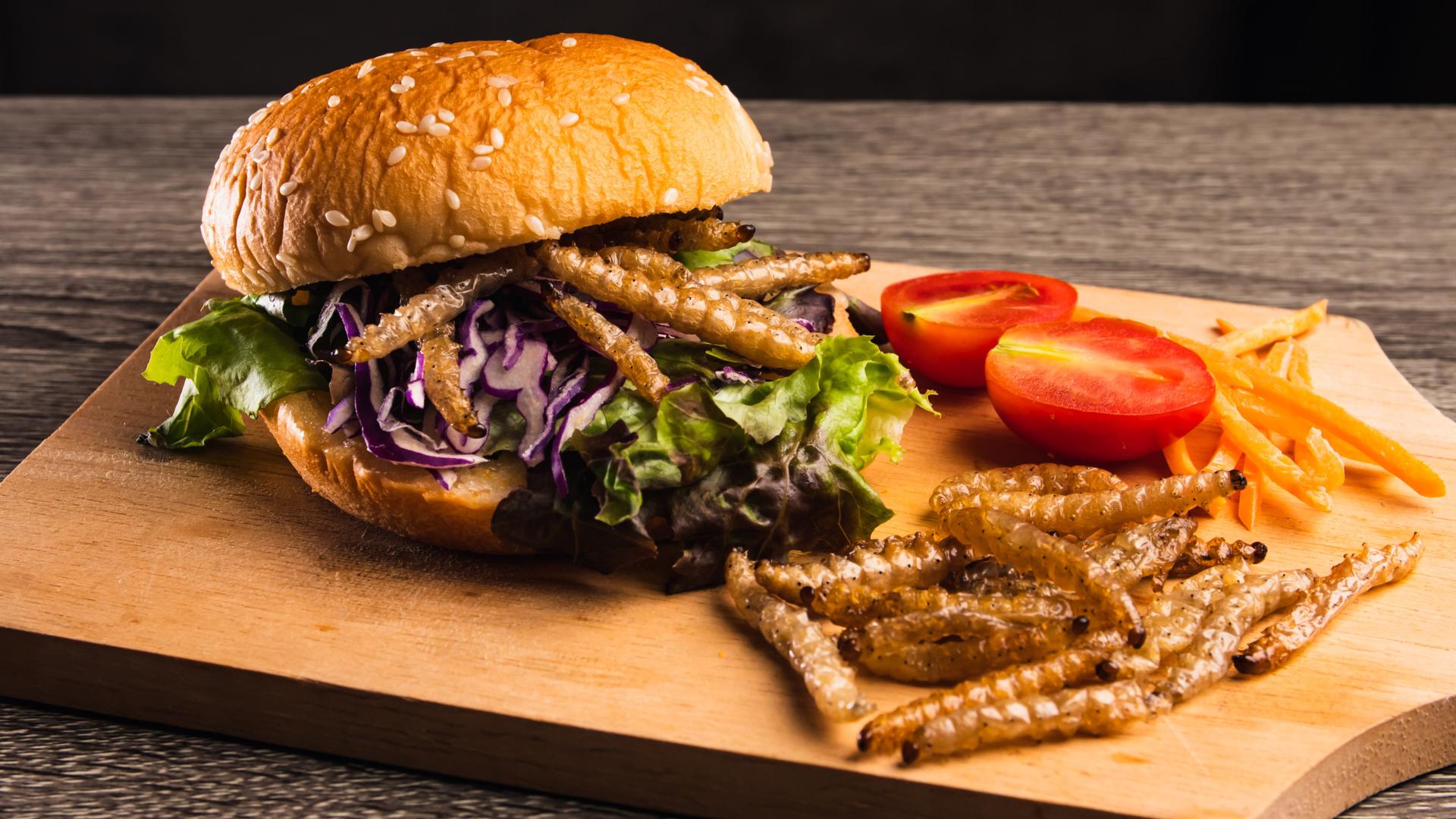Hamburger mit gebratenen Bambusraupen und Gemüsesalat auf Holzteller.