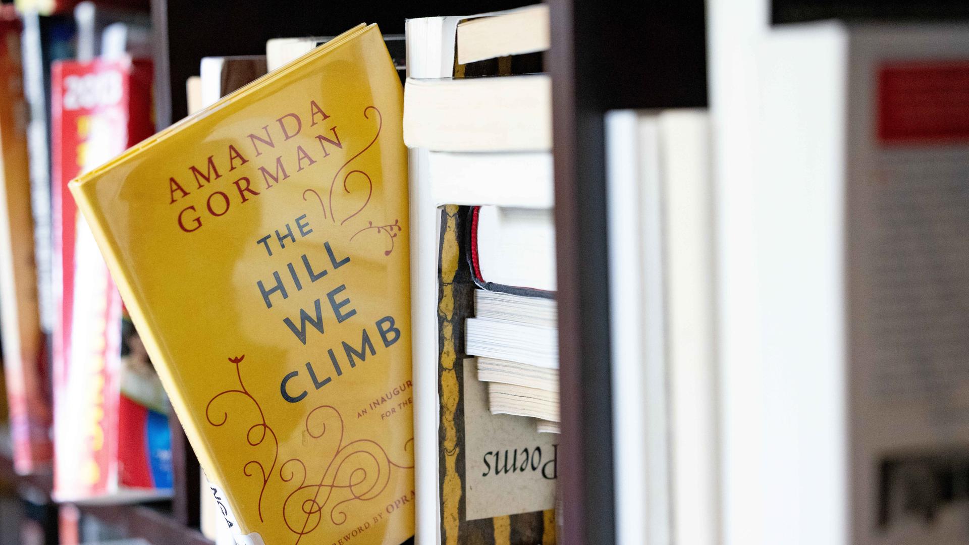 Ein gelbes Buch mit dem englischen Titel "The hill we climb" scheint fast aus einem Bücherregal herauszufallen Ein gelbes Buch mit dem englischen Titel "The hill we climb" scheint fast aus einem Bücherregal herauszufallen