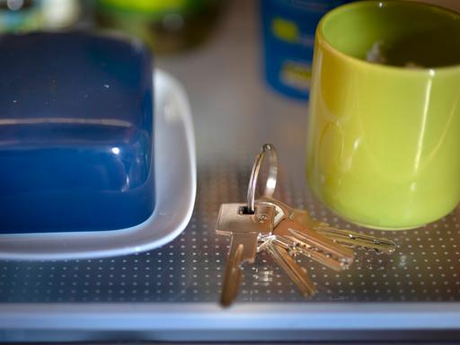 In einem Kühlschrank liegt neben einer blauen Butterdose und einer grünen Tasse ein Schlüsselbund.