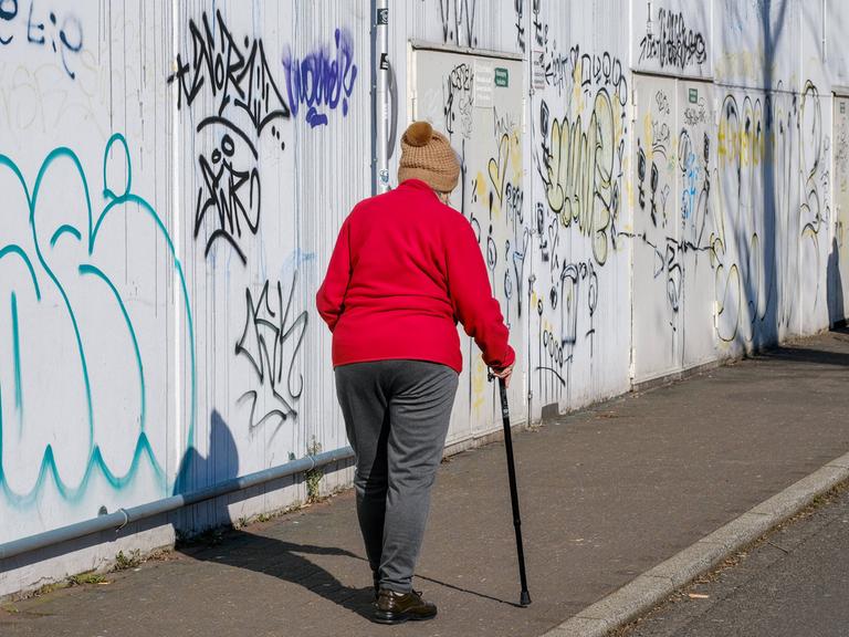 Alter Mensch mit Stock vor einer Graffiti-Wand 