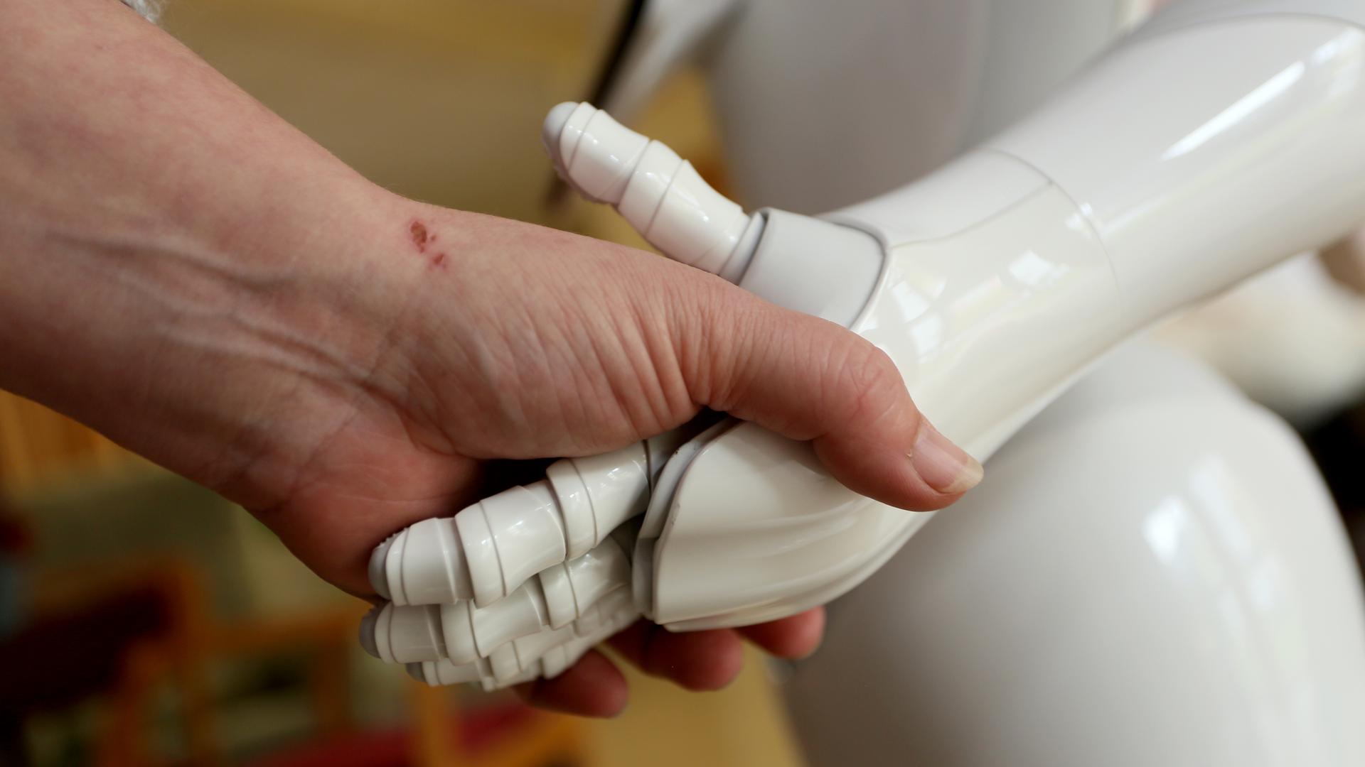 Eine menschliche Hand umfasst die Hand eines Roboters. Eine menschliche Hand umfasst die Hand eines Roboters.