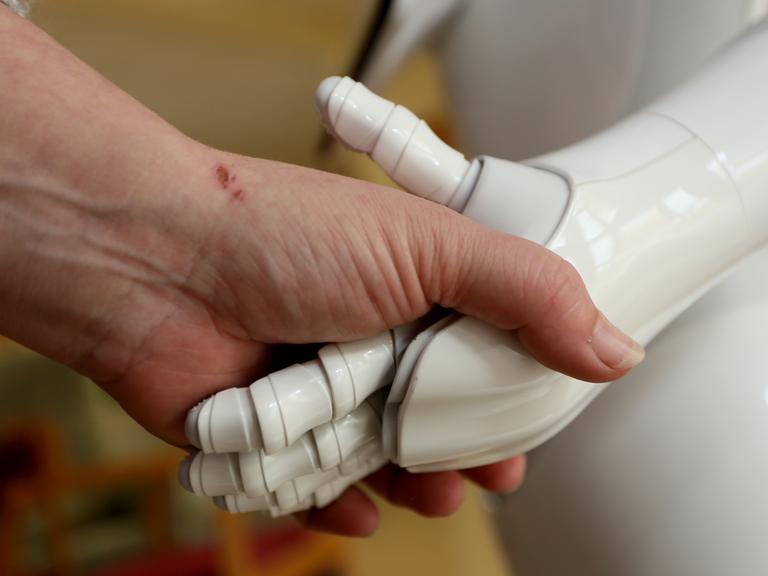 Eine menschliche Hand umfasst die Hand eines Roboters.