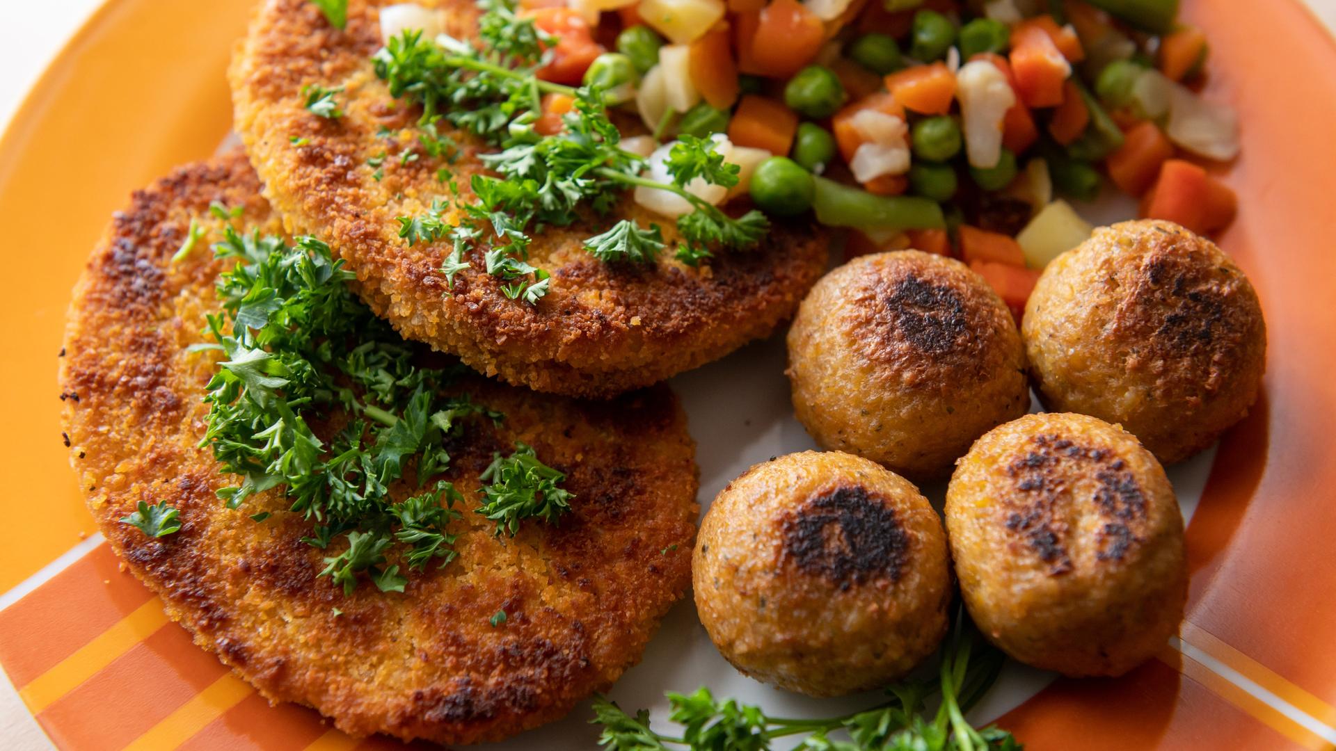 Vegane Falafel, vegane Schnitzel und Gemüse liegen auf einem Teller.