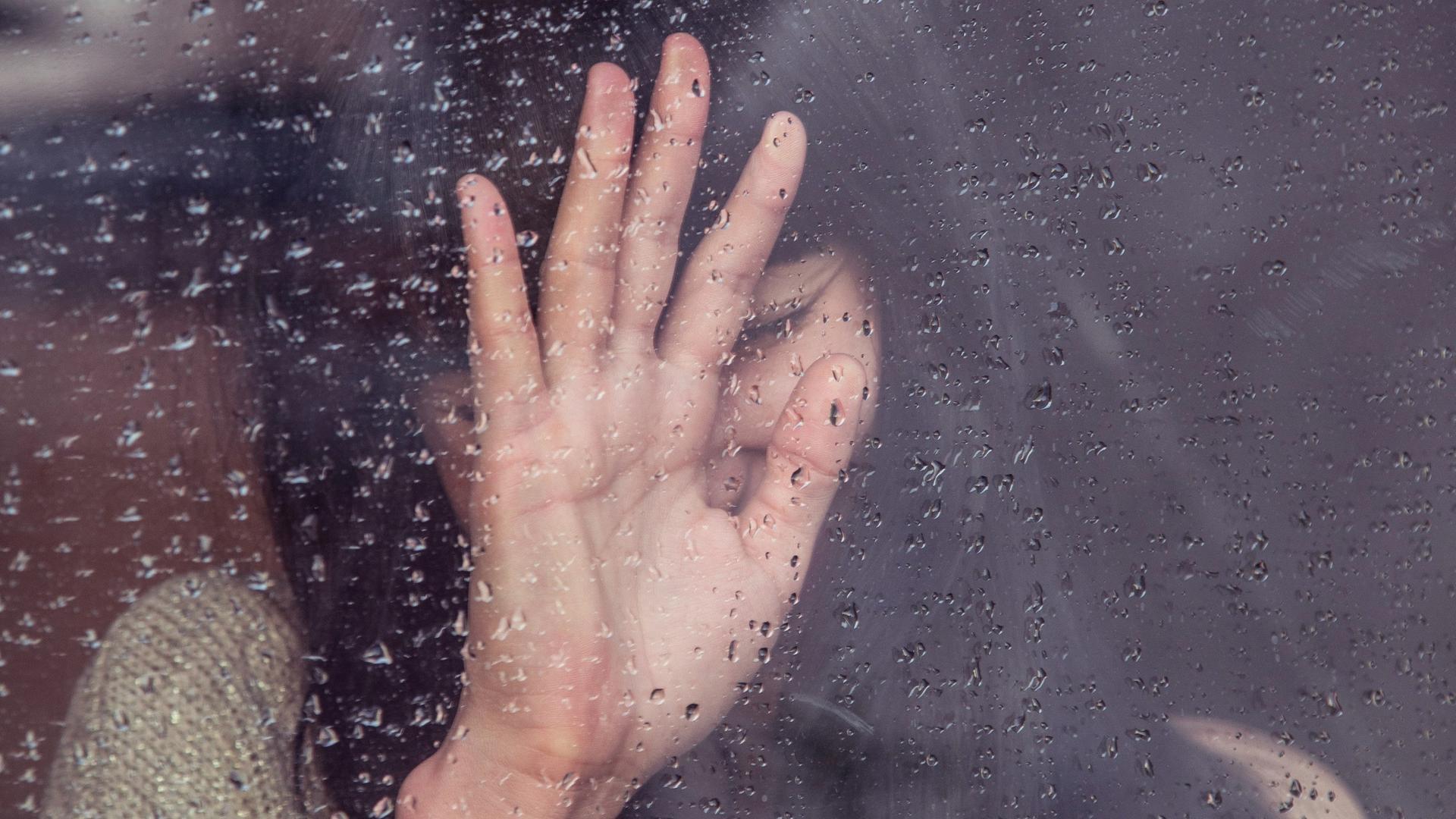 Eine trauernder Frau steht an einer verregneten Scheibe, an die sie ihre Hand drückt Eine trauernder Frau steht an einer verregneten Scheibe, an die sie ihre Hand drückt