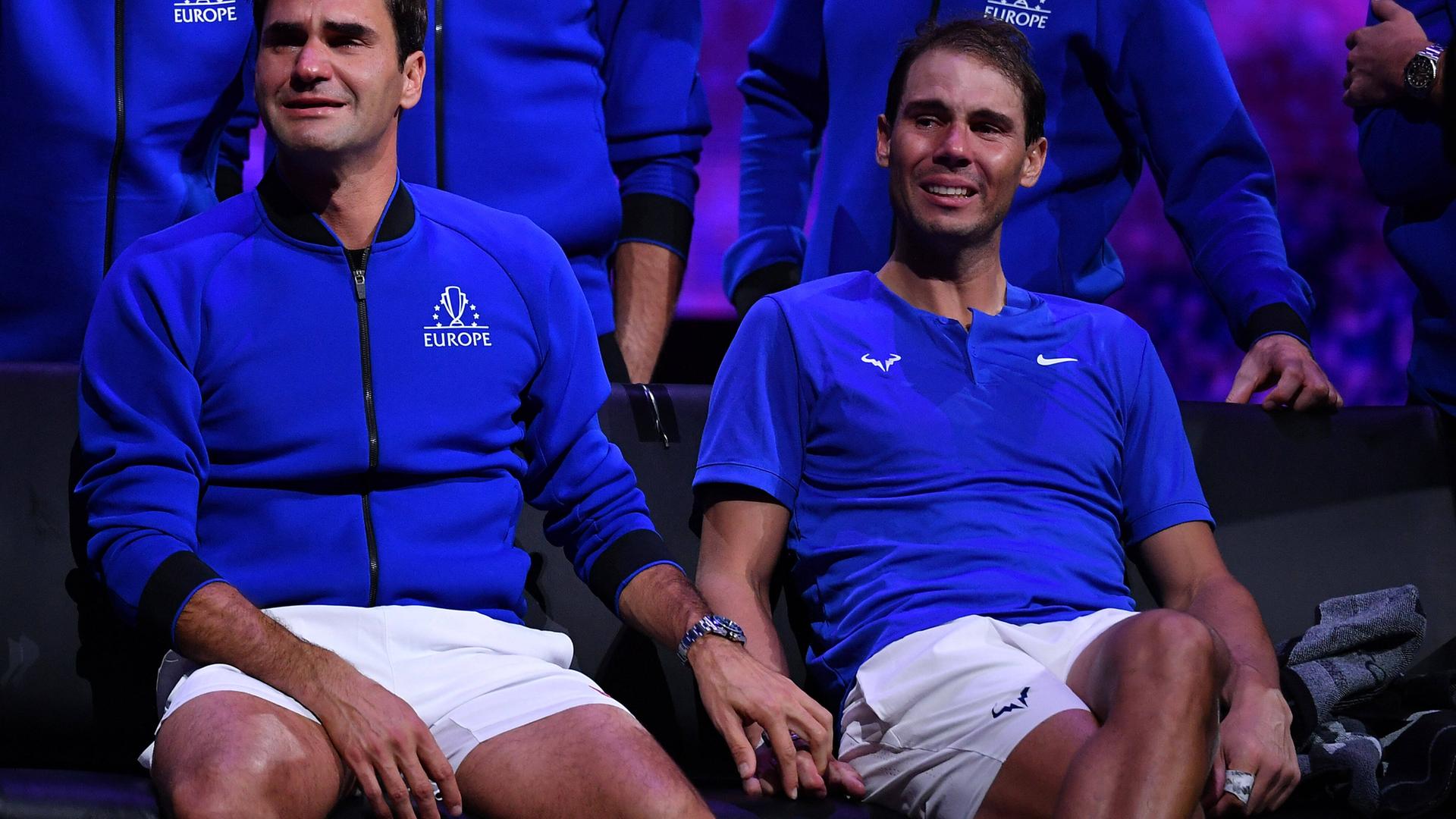 Federer und Nadal sitzen weinend in blauen Oberteilen auf eine Bank und Federer legt seine Hand auf Nadals. Federer und Nadal sitzen weinend in blauen Oberteilen auf eine Bank und Federer legt seine Hand auf Nadals.