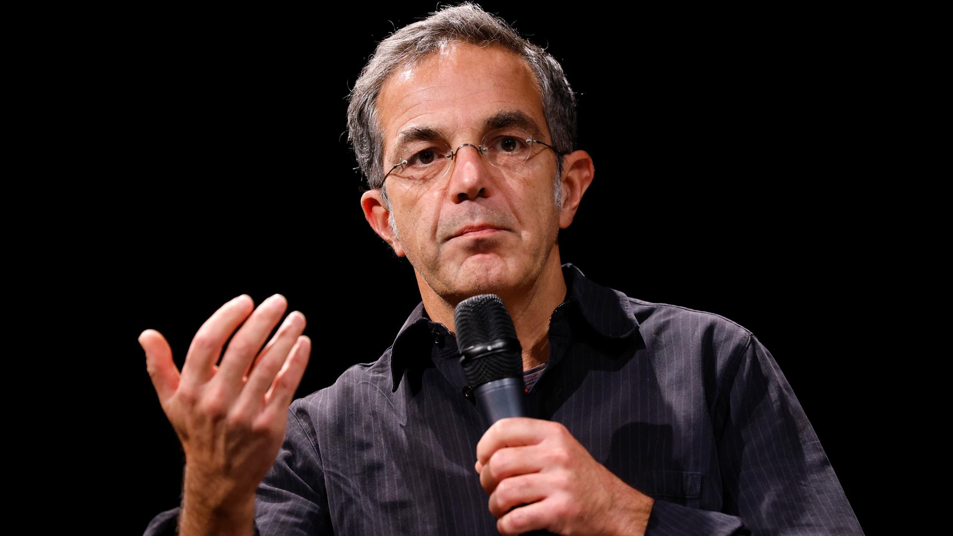 Der Schriftsteller Navid Kermani. Der 55-Jährige Mann mit Brille hält ein Mikrofon. Der Schriftsteller Navid Kermani. Der 55-Jährige Mann mit Brille hält ein Mikrofon.
