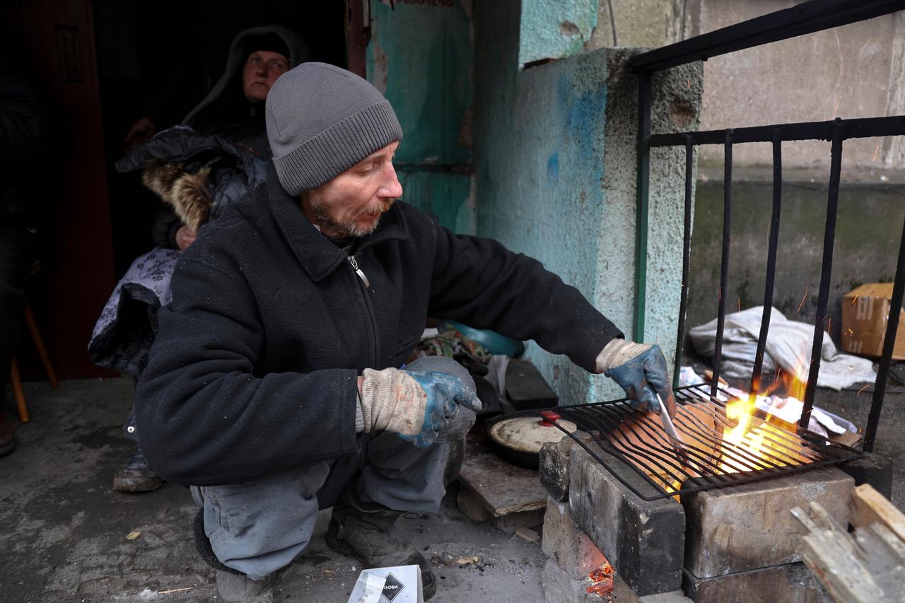 Ein Mann bereitet in Mariupol Essen am Eingang eines Gebäudes zu, das während der Kämpfe beschädigt wurde.