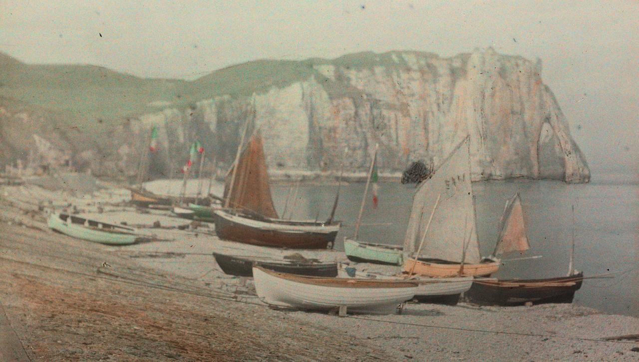 Eine frühe Fotografie von Booten, die auf einem Strand liegen vor einer Felsenküste.