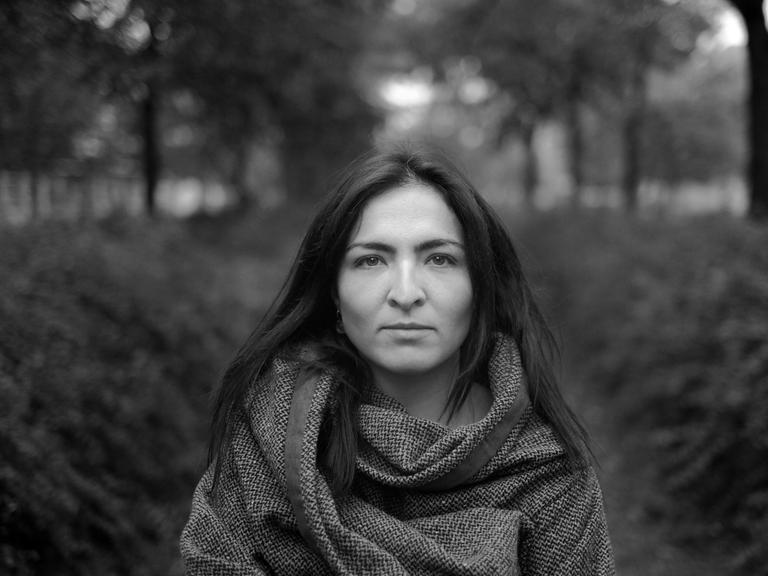 Porträt von Petya Lund in schwarz-weiß. Zu sehen ist eine junge Frau eingehüllt in einen Schal in einer Flucht von Bäumen stehend.