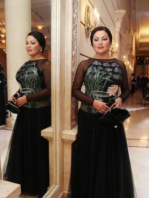 Die Sopranistin Anna Netrebko steht im November 2020 in festlicher Kleidung vor einem Spiegel im Bolschoi-Theater, in dem sie auch von der anderen Seite zu sehen ist.