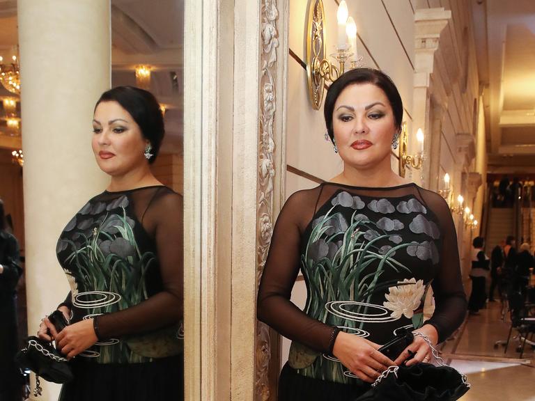 Die Sopranistin Anna Netrebko steht im November 2020 in festlicher Kleidung vor einem Spiegel im Bolschoi-Theater, in dem sie auch von der anderen Seite zu sehen ist.