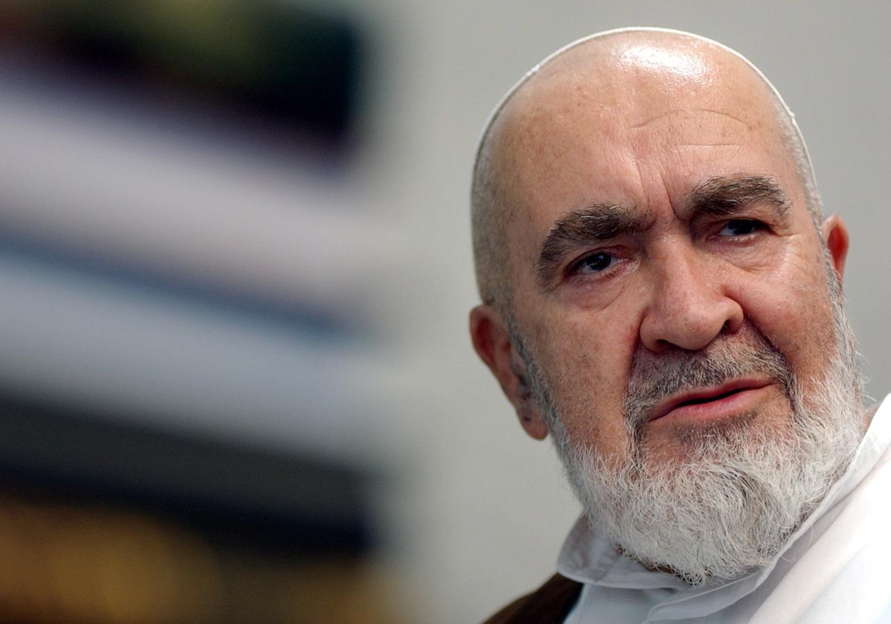 Hossein Ali Montazeri, mit glatt rasiertem Kopf und weißem Bart, schaut ernst zur Seite. Hossein Ali Montazeri, mit glatt rasiertem Kopf und weißem Bart, schaut ernst zur Seite.