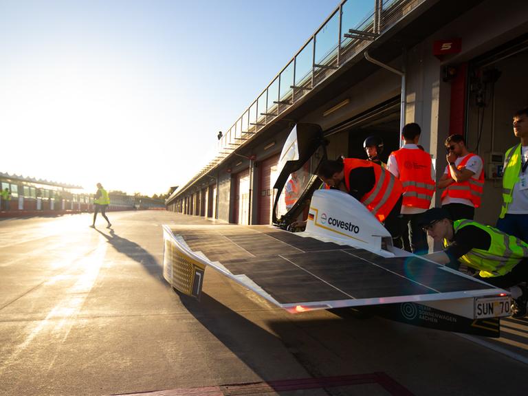 Das Vorläufer-Sonnenmobil des Aachener Teams Sonnenwagen bei einem Rennen. Zu sehen ist das windschnittige Mobil auf einer Rennstrecke, im Hintergrund die Sonne im Dämmerlicht. 