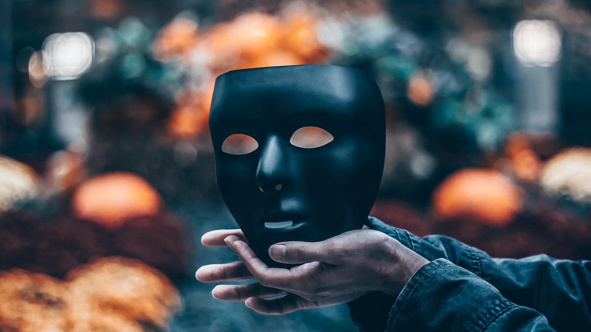 Zwei Hände halten eine schwarze Maske. Zwei Hände halten eine schwarze Maske.