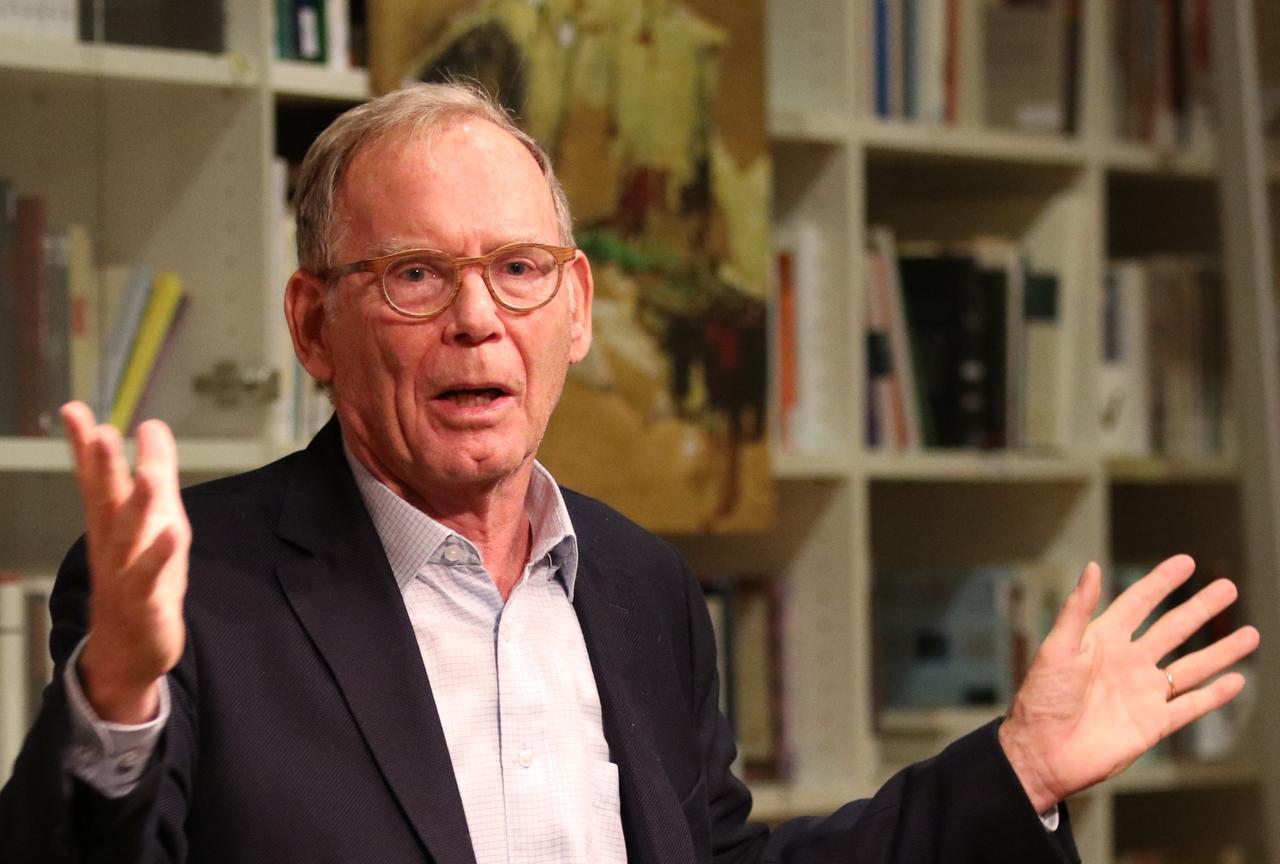 Jens-Uwe Martens, im weißen Hemd mit schwarzem Sakko, steht vor einer Bücherwand und breitet die Arme zu einer erklärenden Geste aus. Jens-Uwe Martens, im weißen Hemd mit schwarzem Sakko, steht vor einer Bücherwand und breitet die Arme zu einer erklärenden Geste aus.