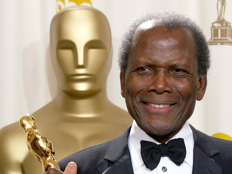 Der schwarze Schauspieler Sidney Poitier steht neben einer großen Oscar-Statue und hält einen Oscar in der Hand