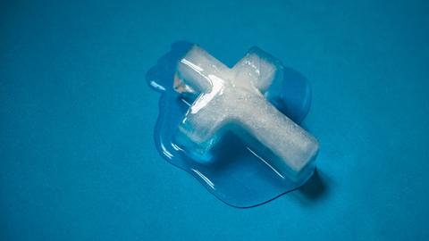 Ein schmelzendes Kreuz aus Eis vor blauem Hintergrund.