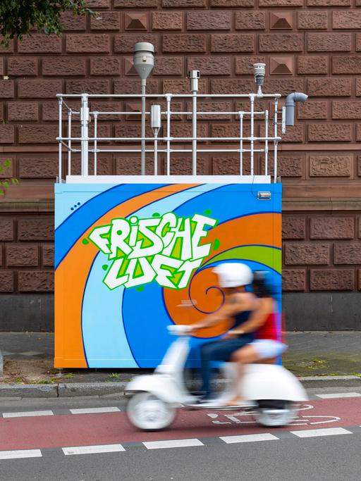 Luftmessstation am Friedrichsring in Mannheim mit Graffiti "Frische Luft" und einem passierenden Roller in der Bewegungsunschärfe. 