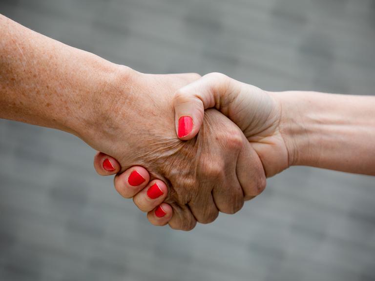 Zwei Menschen geben sich die Hand. 