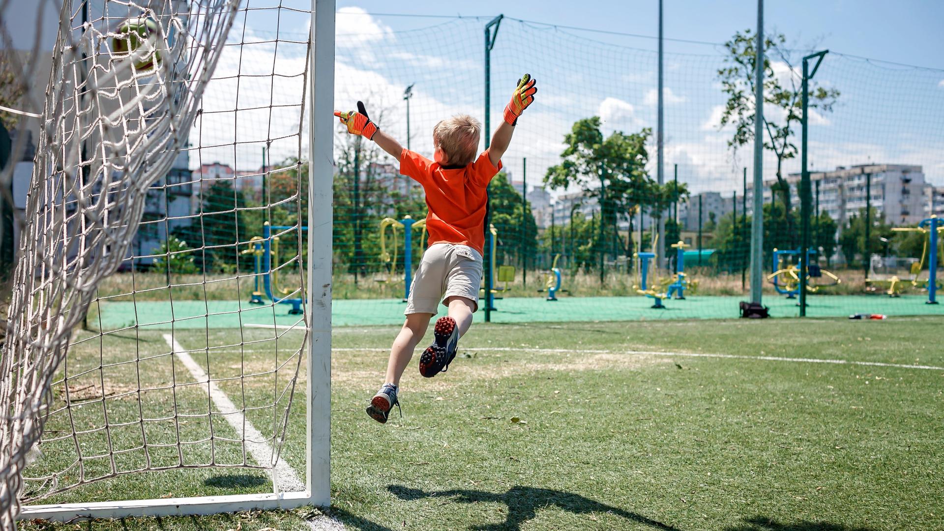 Ein Kind in Fußballkleidung beim Sprung durch die Luft vor einem Tor. Ein Kind in Fußballkleidung beim Sprung durch die Luft vor einem Tor.