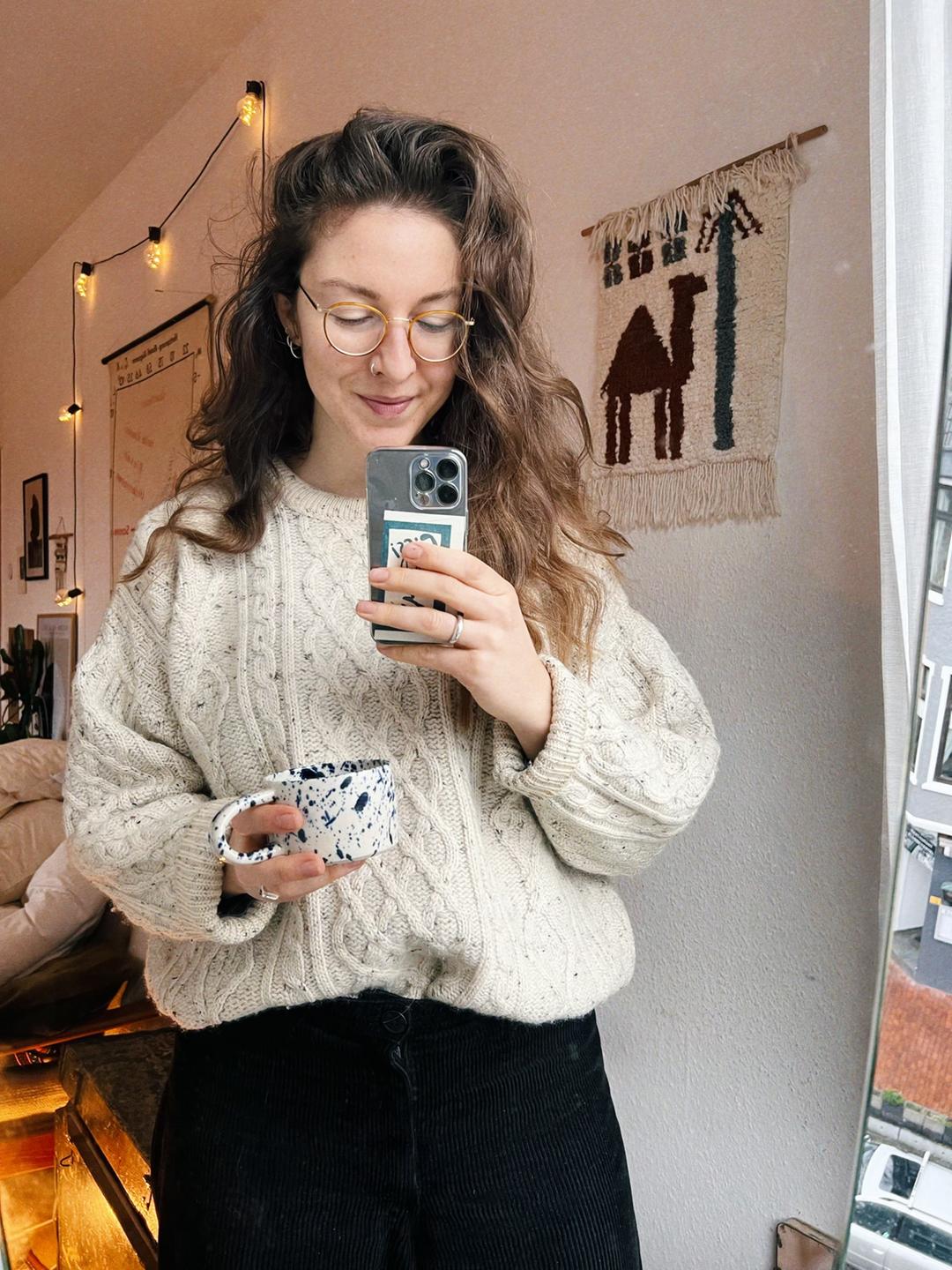 Eine junge Frau schaut auf ihr Smartphone, in der anderen Hand trägt sie eine Tasse: Influencerin Charlotte Wiesiolek. Eine junge Frau schaut auf ihr Smartphone, in der anderen Hand trägt sie eine Tasse: Influencerin Charlotte Wiesiolek.