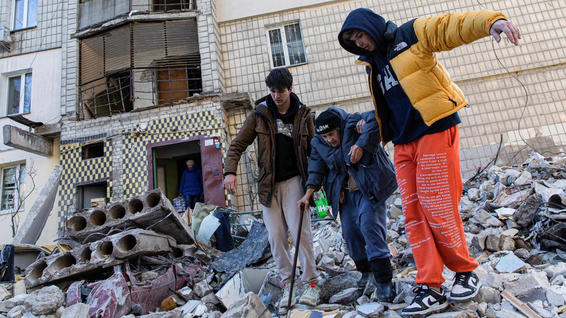 Zwei Männer helfen einer alten Frau in Kiew, ein zerstörtes Gebäude zu verlassen.