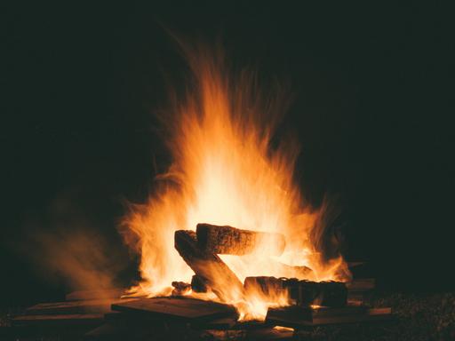 Blick auf ein großes Lagerfeuer mit glühenden Holzscheiten in der Nacht.