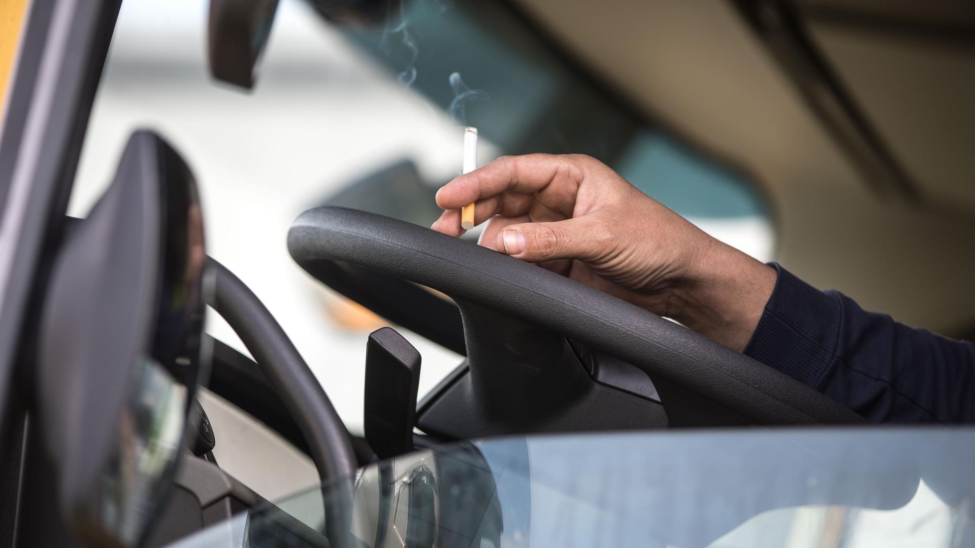 Ein Mann hat seine Hand auf dem Lenkrad eines Lkw abgelegt. Er hält eine Zigarette zwischen den Fingern. Ein Mann hat seine Hand auf dem Lenkrad eines Lkw abgelegt. Er hält eine Zigarette zwischen den Fingern.