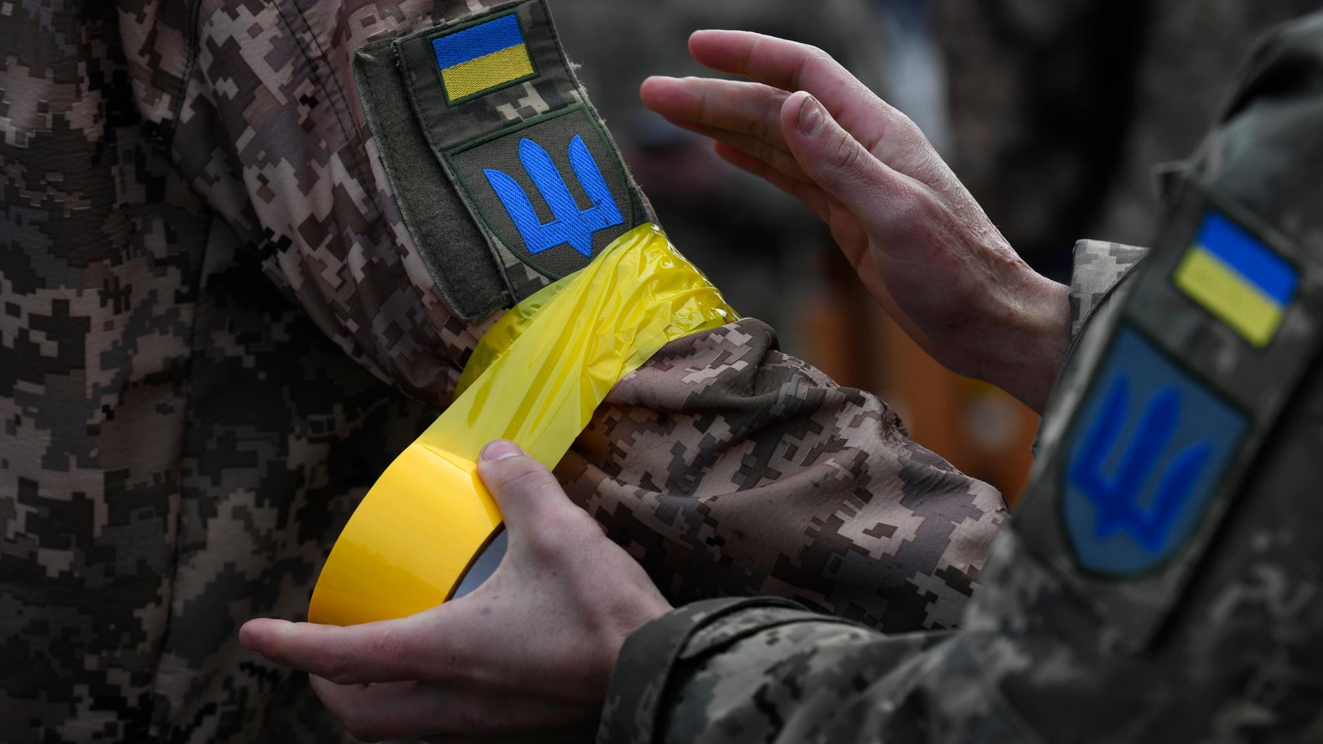 Ein ukrainischer Soldat macht einem Kameraden gelbes Klebeband an den Arm als Zeichen der Zugehörigkeit zu den regulären Streitkräften. Ein ukrainischer Soldat macht einem Kameraden gelbes Klebeband an den Arm als Zeichen der Zugehörigkeit zu den regulären Streitkräften.