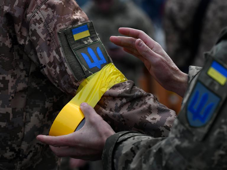 Ein ukrainischer Soldat macht einem Kameraden gelbes Klebeband an den Arm als Zeichen der Zugehörigkeit zu den regulären Streitkräften.