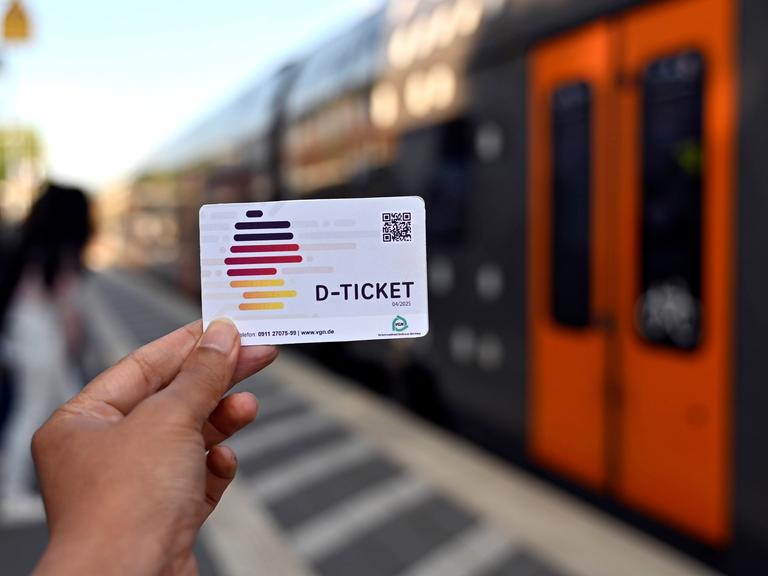 Eine Hand hält ein Deutschland-Ticket vor eine Zugtür der Deutschen Bahn. 