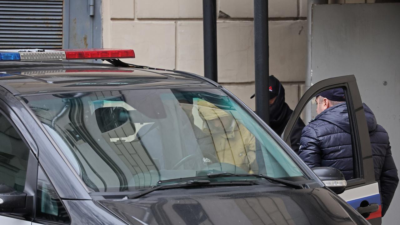 Evan Gershkovich in einer gelben Jacke, wie er von zwei Beamten in ein Polizeiauto verladen wird.