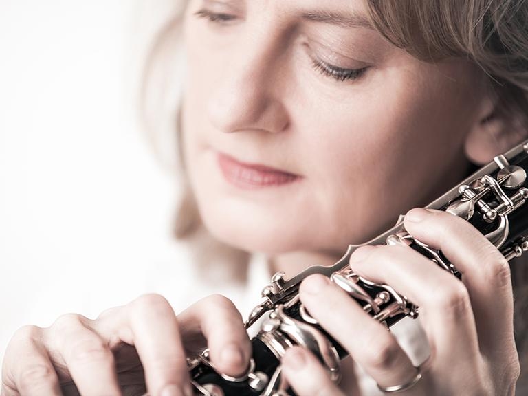 Sabine Meyer hält ihre Klarinette vor ihr Gesicht und schaut auf ihre Hände, die die Klarinette umfassen.