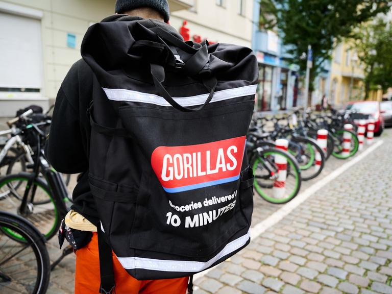 Ein Beschäftigter des Lieferdienstes Gorillas trägt einen Rucksack und steht vor den Fahrrädern. 
