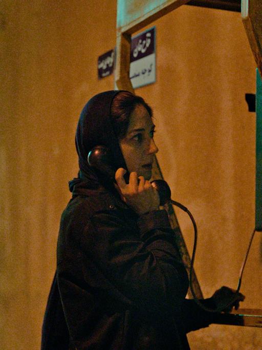 Filmstill aus dem Film "Holy Spider": Eine Frau mit Kopftuch telefoniert an einer Telefonzelle. 