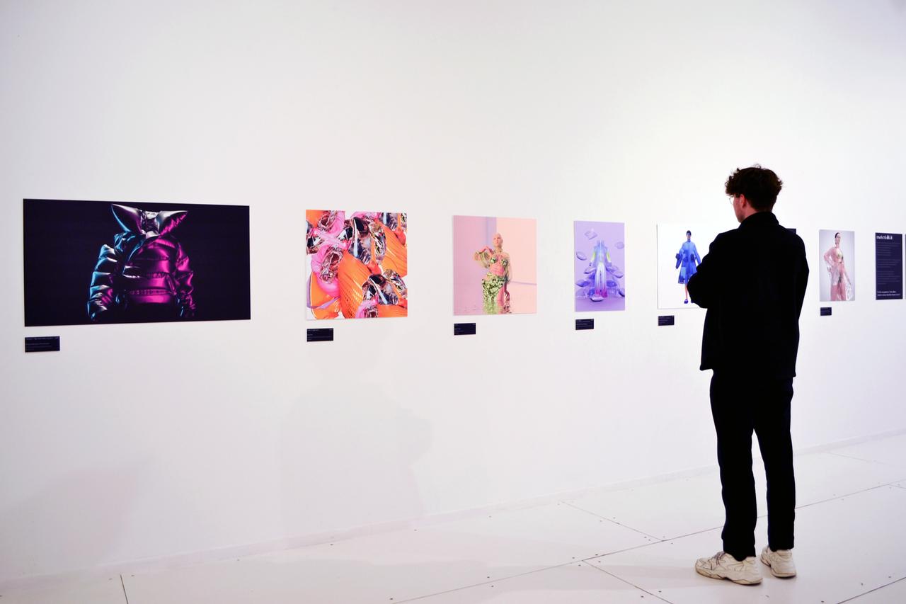 Ein Besucher der Ausstellung "virtuelles Beiwerk" steht vor einer Wand mit Drucken.
