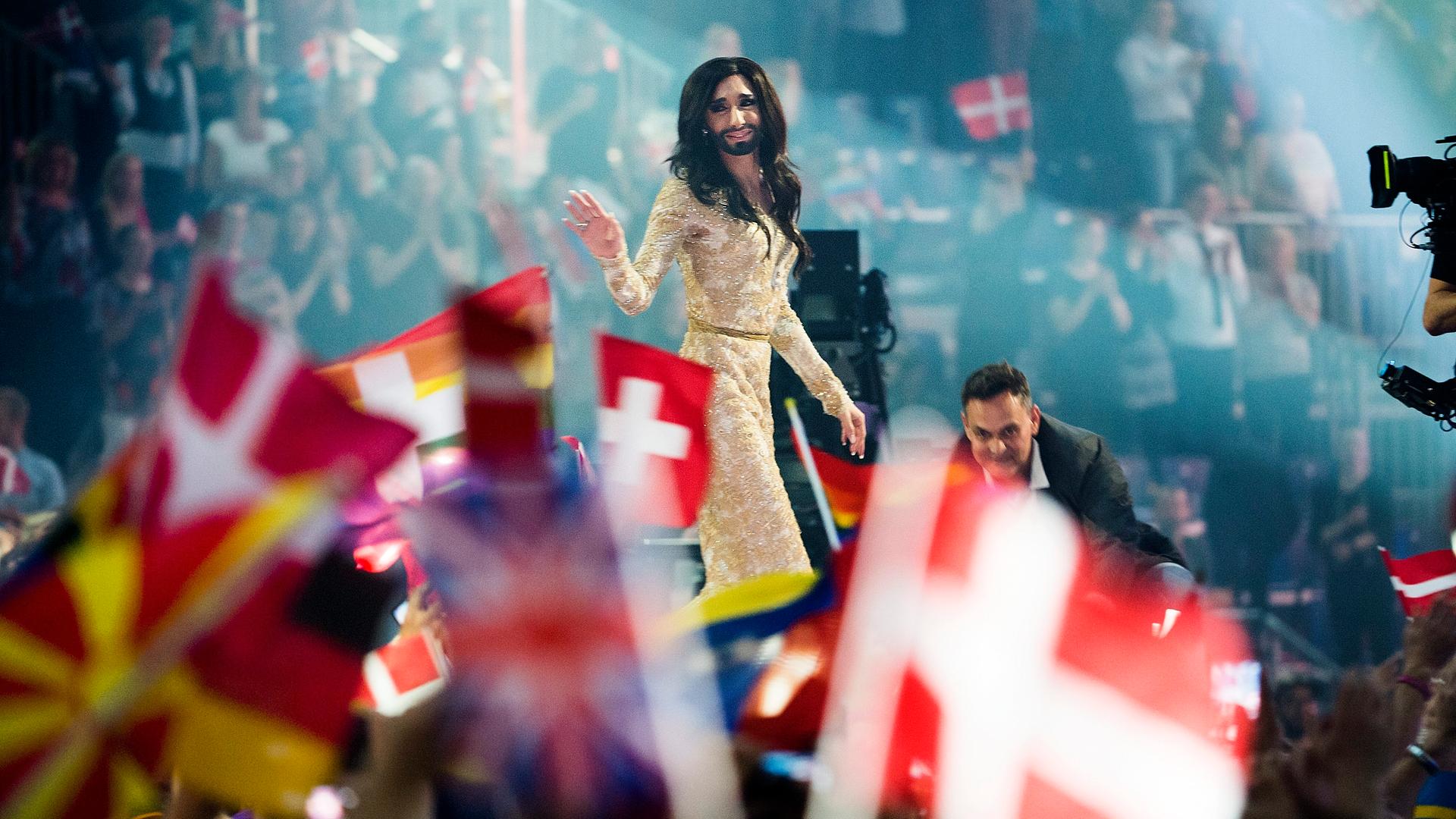 Beim 59. Eurovision Song Contest (ESC) in Kopenhagen 2014 lässt sich Conchita Wurst nach dem Sieg auf der Bühne feiern, im Vordergrund sind Flaggen verschiedener Länder zu sehen. Beim 59. Eurovision Song Contest (ESC) in Kopenhagen 2014 lässt sich Conchita Wurst nach dem Sieg auf der Bühne feiern, im Vordergrund sind Flaggen verschiedener Länder zu sehen.
