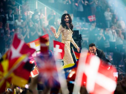 Beim 59. Eurovision Song Contest (ESC)  in Kopenhagen 2014 lässt sich Conchita Wurst nach dem Sieg auf der Bühne feiern, im Vordergrund sind Flaggen verschiedener Länder zu sehen.