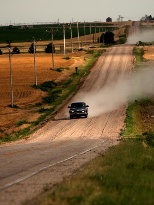 Ein einsamer Pickup Truck fährt eine ländliche Straße im US-Bundesstaat Colorado entlang und wirbelt eine Staubwolke auf.