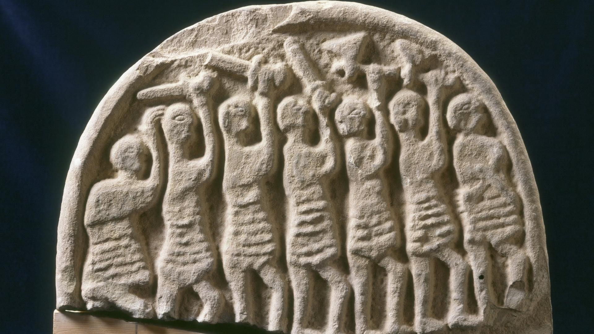 In einen Stein sind mehrere bewaffnete Krieger eingeritzt, die ihre Schwerter in die Luft recken.