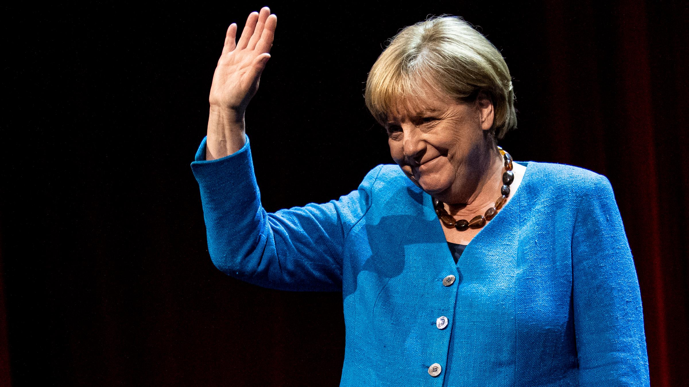 Ex-Kanzlerin Merkel winkt im blauen Blazer in die Kamera.