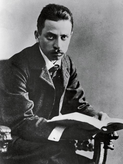 Schwarzweißporträt von Rainer Maria Rilke, der von einem aufgeschlagenen Buch aufblickt.