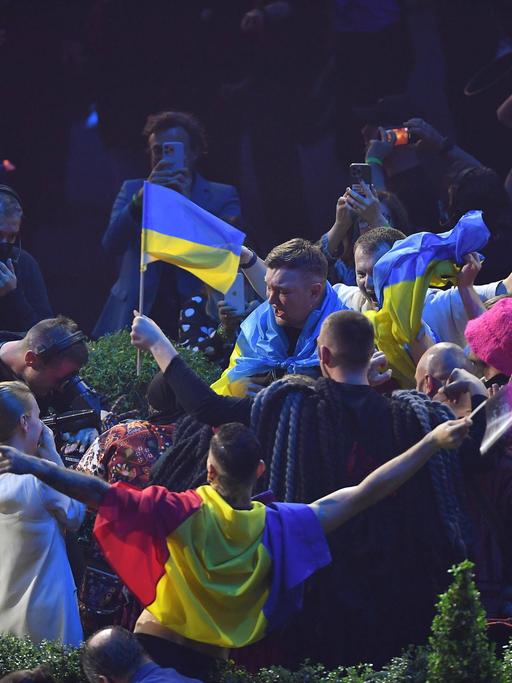 Die Band Kalush Orchestra aus der Ukraine feiert nach dem Sieg beim Eurovision Song Contest 2022. Ukrainische Fahnen werden geschwenkt, es wird gefilmt und fotografiert.  