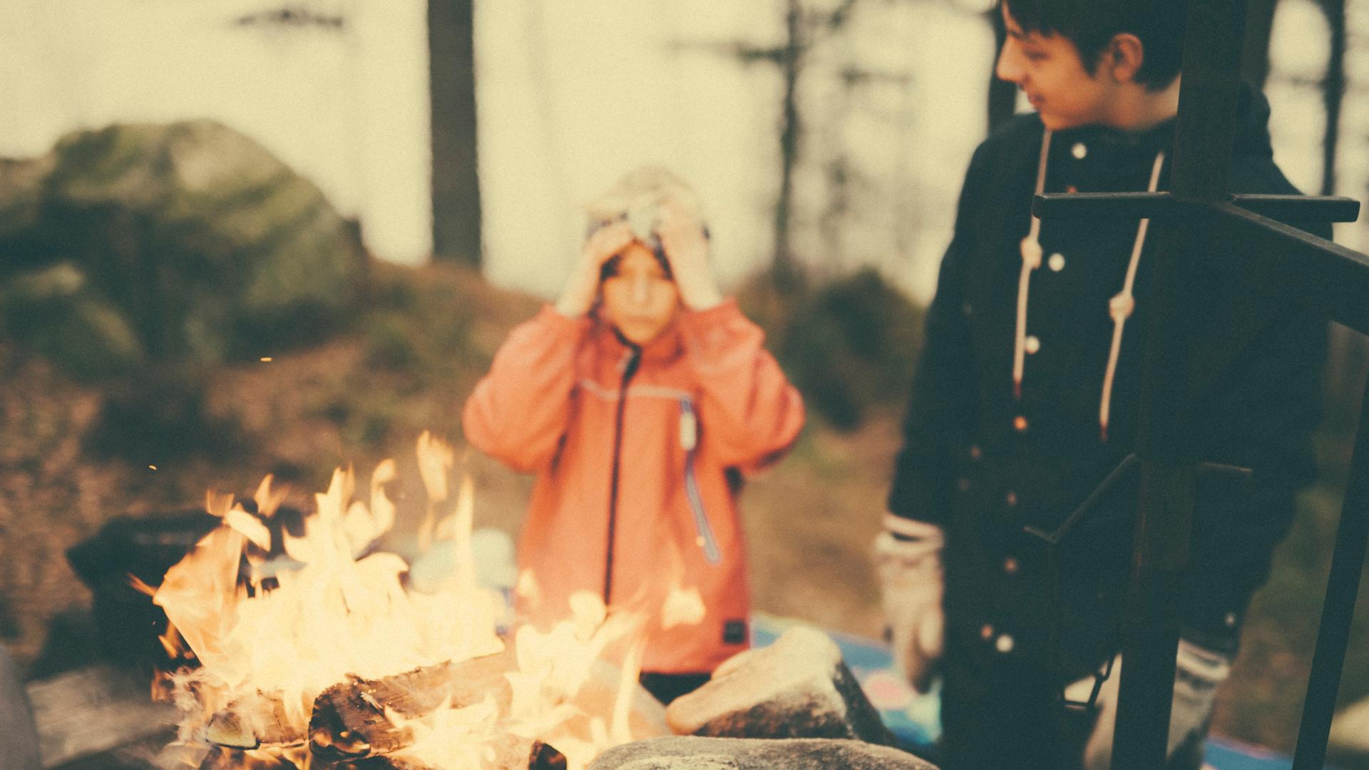 Ein Junge und ein junger Mann stehen vor einem Lagerfeuer.