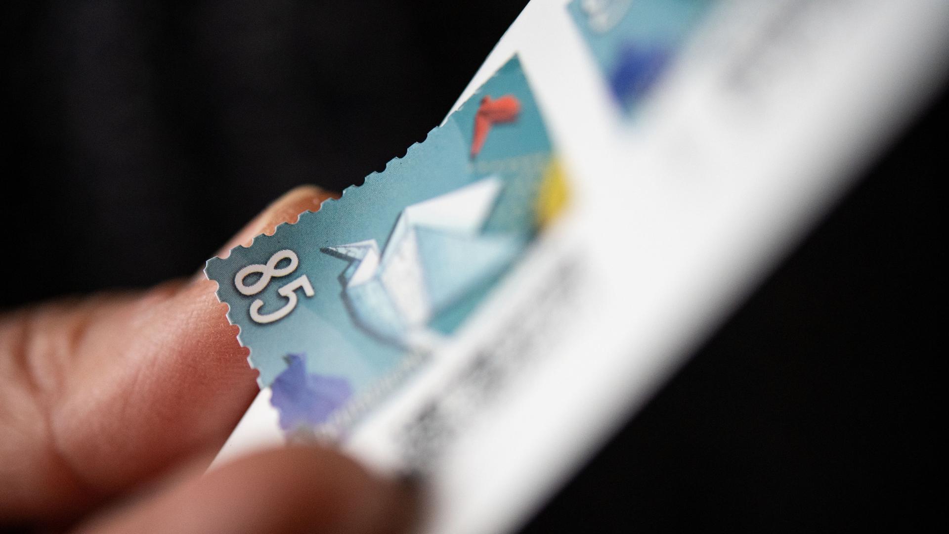 Eine Frau löst eine 85 Cent Briefmarke von einem Bogen. Eine Frau löst eine 85 Cent Briefmarke von einem Bogen.