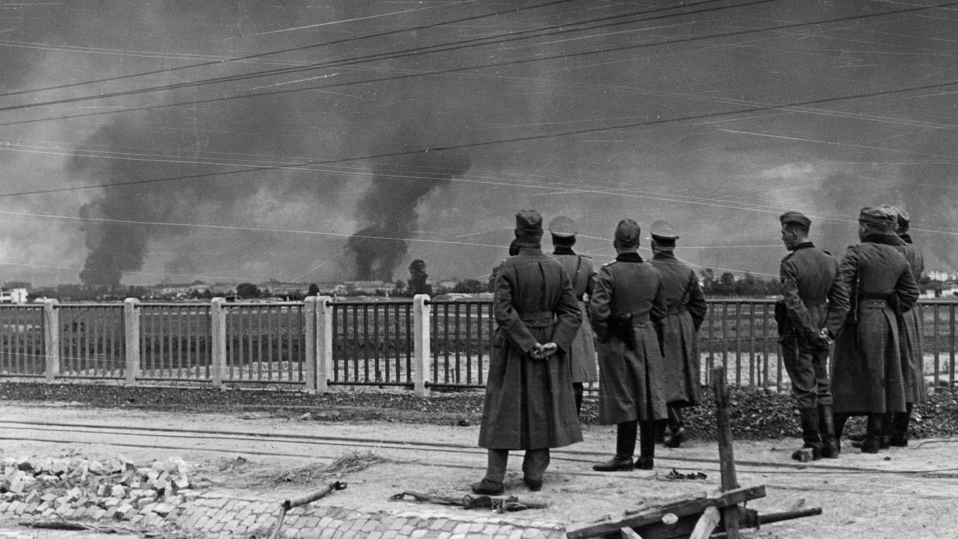 Im Vordergrund stehen deutsche Soldaten der Wehrmacht und beobachten die Angriffe auf Warschau. Im Vordergrund stehen deutsche Soldaten der Wehrmacht und beobachten die Angriffe auf Warschau.