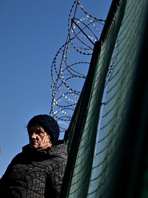 Eine geflüchtete Person lehnt erschöpft am Grenzzaun
