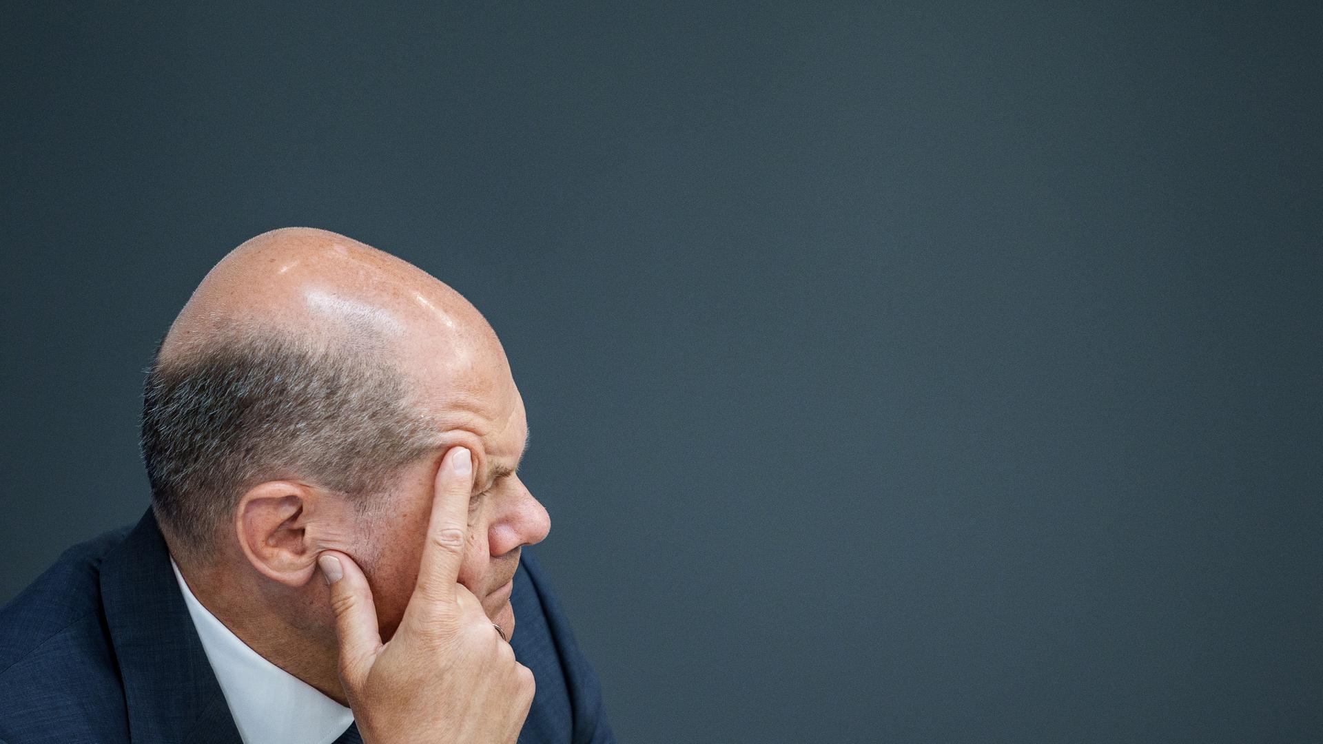Bundeskanzler Olaf Scholz hat sein Gesicht nachdenklich in seine Hände gestützt und verfolgt eine Debatte im Bundestag.