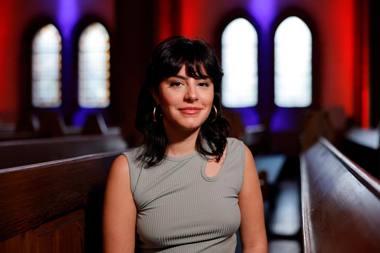 Şeyda Kurt sitzt auf einer Kirchenbank und lacht in die Kamera. Şeyda Kurt sitzt auf einer Kirchenbank und lacht in die Kamera.